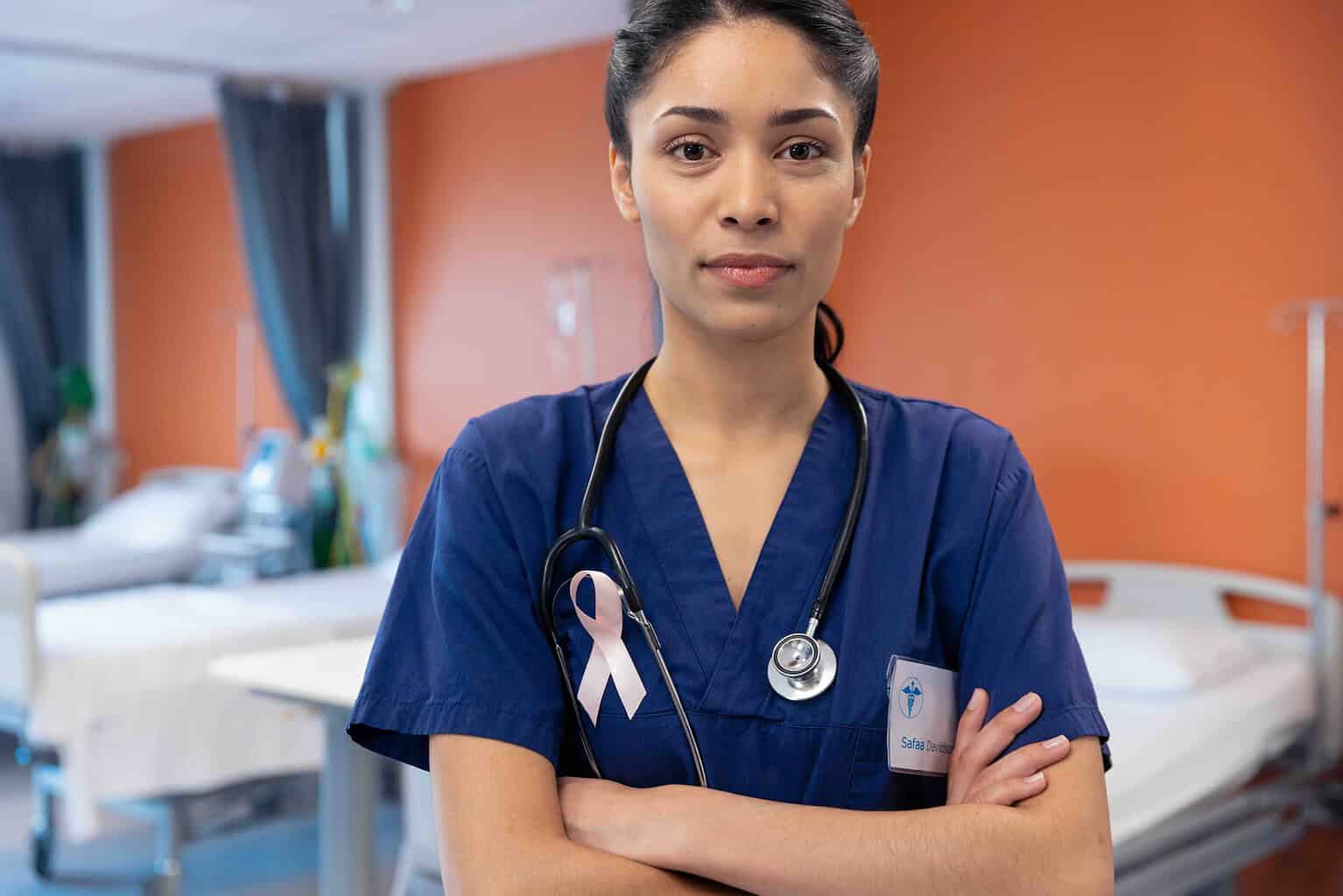 Portrait of biracial female doctor wearing cancer ribbon in hospital ward, copy space. Hospital, medical and healthcare services.